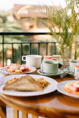 Beautiful exotic breakfast on a wooden table. Plates with fruit, scrambled eggs, cups of tea. Side view, in the background palm tree.