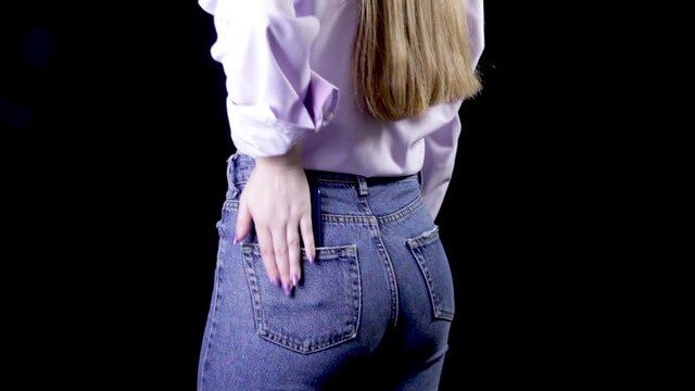 Woman puts mobile phone in jeans pocket on black background.