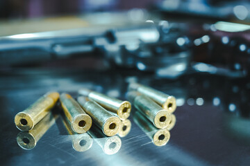 Air gun with bullets lies on a metal tray close-up. Pneumatic revolver with gold cartridges lies on a silver shiny surface