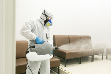 Worker wearing (ppe) protective equipment suit, gloves, mask, and chemical mask cleaning the room with machine of pressurized spray disinfectant water to remove covid-19 coronavirus. - obrazy, fototapety, plakaty