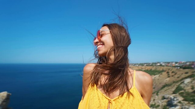 closeup clow motion portrait beautiful young smiling brunette woman with long wind blowing hair. girl wearing in orange sundress and sunglasses, wind flying hair to camera