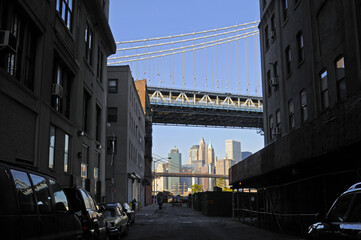 Vue en clair-obscur sur une rue de brooklyn donnant sur le pont de manhattan, le matin au lever du soleil et jeu de reflet du ciel sur les vitres des bâtiments et voitures.