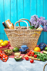 Homemade picnic with fresh fruits, vegetables, salad, orange juice, flowers and baguette in wicker basket. Beautiful still life