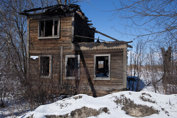 an old unkept abandonned traditonal russian wooden two floor house in ruins in winter snow surrounded by naked birch trees and branches. Shot in nothern city of Arkhangelsk, Primorsk region, Russia.