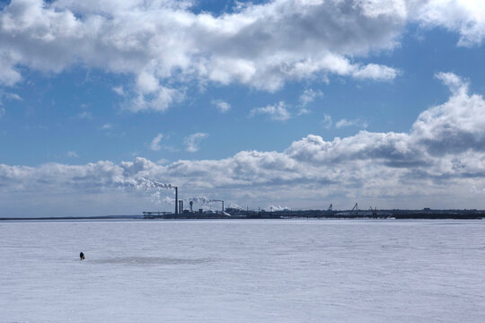 a lonely man crossing with a bag in his hand a frozen sea from one shore to another in wintertime with industrial factories and smoke background near the northern city of Arkhangelsk. Primorsk, Russia