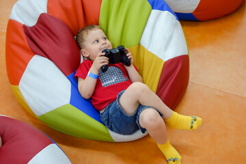 Cute small boy is sitting in the bean bag  armchair and playing