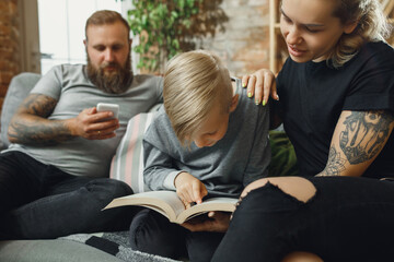 Happy family at home spending time together. Having fun, look cheerful and lovely. Mother, father and son reading book during remote school studying. Parents helping. Childhood, domestic life concept.
