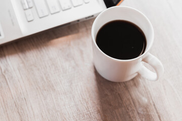 Close up black coffee in white cup and laptop on wooden table. Work from home concept