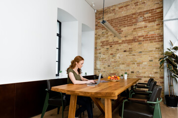 Side view of attractive freelancer using laptop near fruits on table