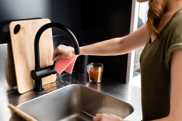 Cropped view of woman holding knife and rag near kitchen sink