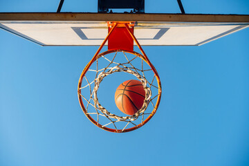 Street basketball ball falling into the hoop. Urban youth game. Close up of orange ball above the hoop net. Concept of success, scoring points and winning