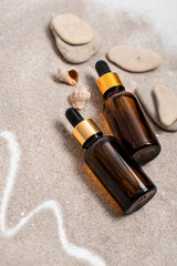 Glass brown bottles of serum with a pipette for skin care is on the sand with stones and shells. Cosmetics with marine components. The concept of health and beauty. minimalism