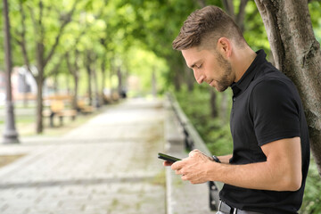 Fototapeta premium Portrait of a trendy young man on a sunny day in the city using cellphone