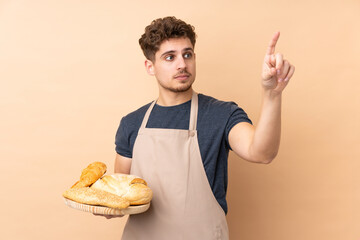 Male baker holding a table with several breads isolated on beige background touching on transparent screen