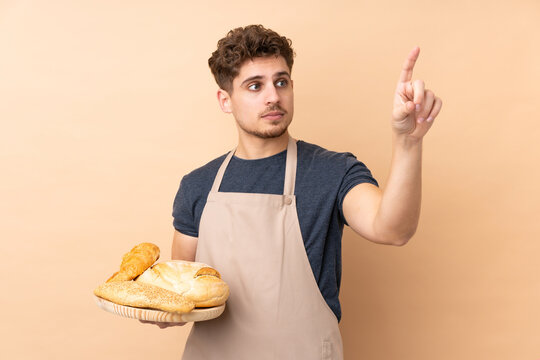 Male baker holding a table with several breads isolated on beige background touching on transparent screen