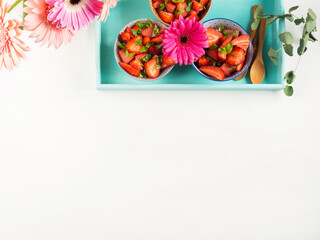 Fruit salad with strawberries, watermelon and basil leaves in ceramic bowls on turquoise wooden tray. Summer healthy snack. Copy space