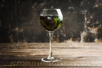 Black cocktail with lime slices in wine glass on the rustic background. Selective focus. Shallow depth of field.