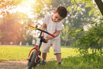 A little boy plays with his bicycle outside in the park on a sunny day.