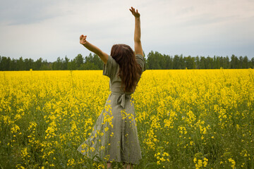 Naklejka na ściany i meble Young woman in sleeveless dress enjoying sunlight and nature on yellow blooming rapeseed field