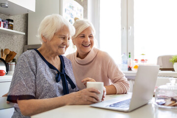 Adult daughter teaching her elderly mother to use laptop
