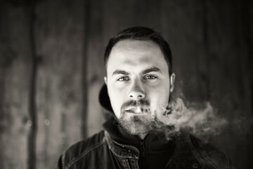 Young man smoking in front of wooden wall