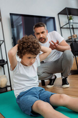 selective focus of curly kid working out on fitness mat near father counting at home