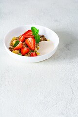 Homemade crunchy granola with nuts, dried fruits, fresh strawberries, mint and yogurt (fermented baked milk) on a white plate. Healthy breakfast concept.