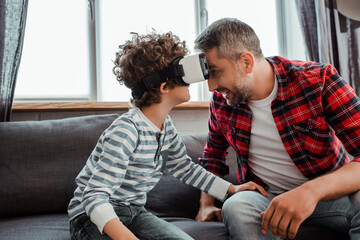 cheerful father near curly son in virtual reality headset