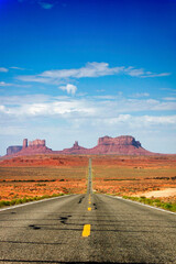 Fototapeta na wymiar Highway in the desert vanishing towards the sunstone buttes of Monument Valley.