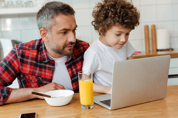 Fototapeta na wymiar handsome father and curly son looking at laptop in kitchen