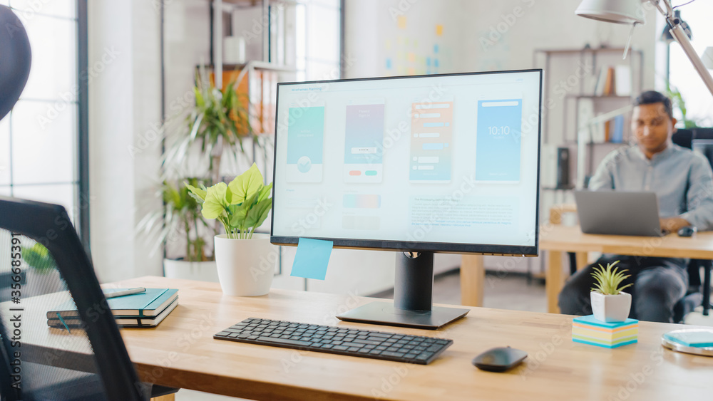 Poster Desktop Computer Standing on the Desk in the Modern Creative Office. Screen Showing Smartphone Application UI / UX.  In the Background Bright Studio with Young Professionals Work on Computers.