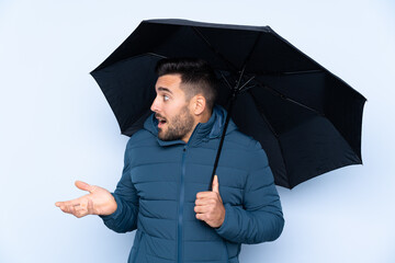 Man holding an umbrella over isolated background with surprise facial expression