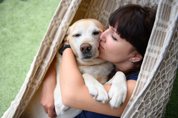 Girl with a dog lies in a hammock. Girl hugs a dog and kisses her.