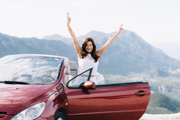 Happy woman stay near red convertible car with a beautiful view