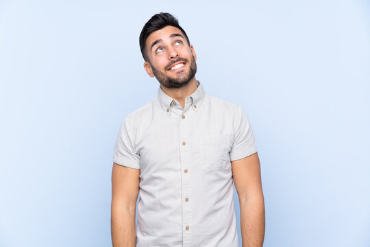Young handsome man with beard over isolated blue background laughing and looking up