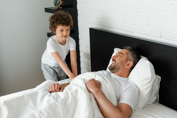 Fototapeta premium curly kid touching happy father lying in bed