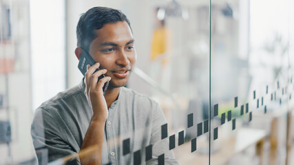 Portrait of Handsome Professional Indian Man Uses Mobile Phone, Talks with Clients and Closes...