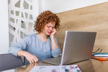 Young frustrated woman working at office desk in front of laptop suffering from chronic daily headaches, treatment online, appointing to a medical consultation, electromagnetic radiation, sick pay