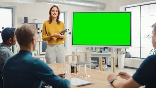 Female Project Manager Holds Meeting Presentation For A Team Of Developers. She Shows Green Screen Interactive Whiteboard Device For Business Planning Concept. Young People Work In Creative Office.