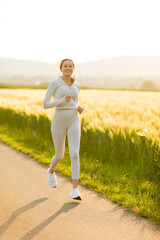 Sportliche junge Frau joggt abends zwischen Feldern