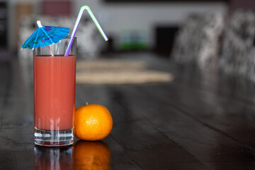 tropical grapefruit juice in a transparent glass on a dark wooden table. Cocktail blue umbrella and orange mandarine.