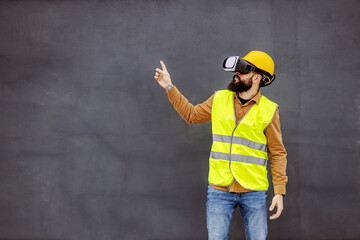 Young bearded constructor in working wear having virtual reality experience and showing up with his...
