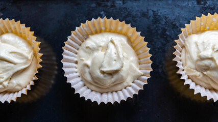Raw batter in cupcake cases waiting to be baked.  Sat on top of dark baking tray centre full focus with further cakes to the side