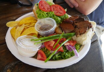 Plate full of beef burger, green vegetable salad, banana chips and dips on a wooden table