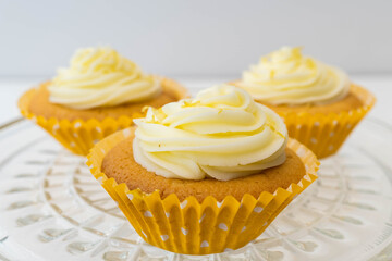 Close up of three cupcakes with frosting sitting on a glass dish with a plain background