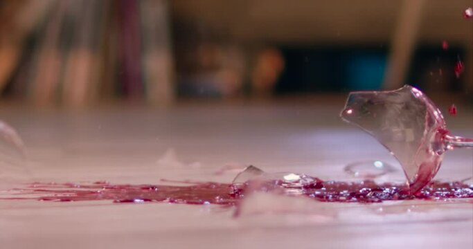 Glass of wine smashing on floor slow motion. Breaking wine glass