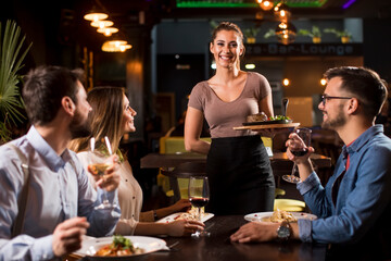 Waiter woman serving group of friends with food in the restaurant