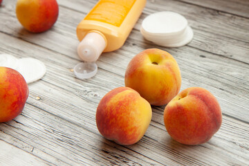 Personal care, cosmetics, cream of peach, ripe peaches, cotton balls for the face on a light wooden background