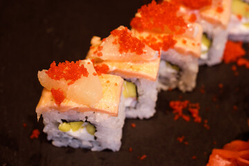 Top view of delicious rice maki with fresh salmon, lemon piece, tobiro ikura, cream cheese and mango. Selective focus on the first roll tobiko top.