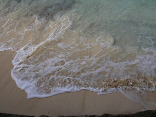 Close up of white foaming waves gently lapping against a soft sandy beach in a tropical island